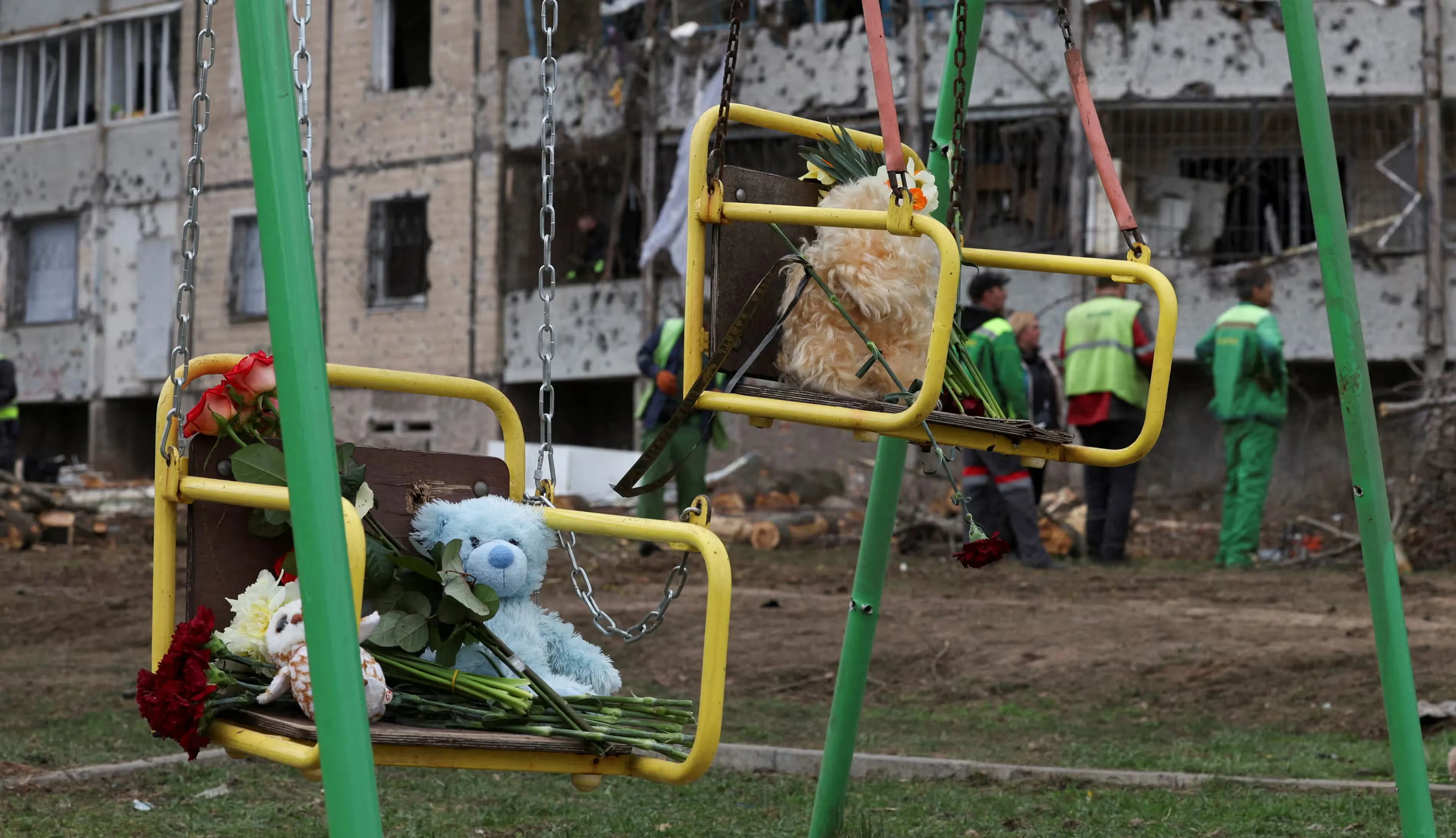 М’які іграшки та квіти ставлять на гойдалках у Кривому Розі, Україна, на місці смертоносного ракетного удару Росії по житловому району в суботу